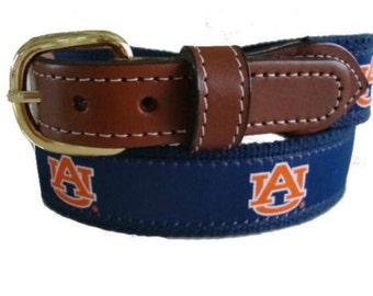 May include: A blue and orange collegiate belt with a leather buckle. The belt features the Auburn University logo.