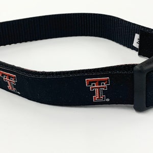 Peut inclure: Collier de chien noir avec un logo "T" rouge et blanc répété sur le collier. Le collier a une boucle en plastique noire et un anneau en D en métal argenté.