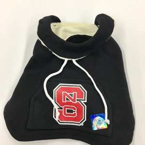 May include: Black hooded sweatshirt with a red and white "NC State" logo on the front. The sweatshirt has a white drawstring and a small pocket on the front.