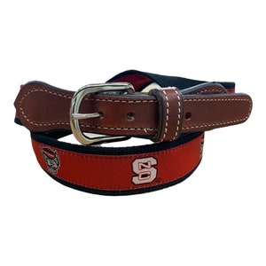 May include: A brown leather belt with a red and black woven strap featuring a white college logo and mascot. The logo is a white letter "S" with a white wolf's head inside the letter.
