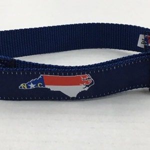 Op de afbeelding: Een blauwe hondenriem met een witte gesp en een bedrukt beeld van de vlag van de staat North Carolina.