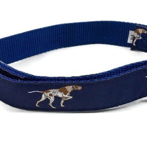 May include: A blue dog collar with a white and brown dog print. The collar has a black buckle and a gold metal D-ring.