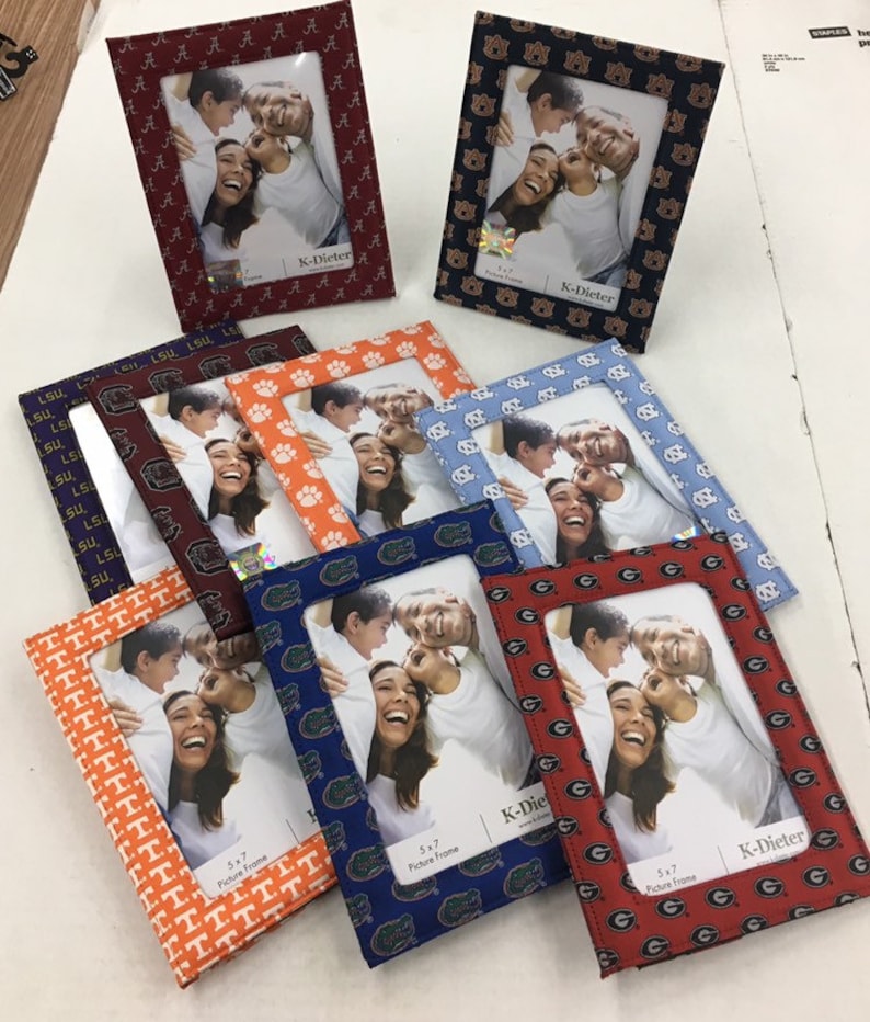 May include: A collection of eight 5x7 inch picture frames with different college team logos. The frames are made of fabric and have a variety of colors and patterns. The frames are all from the same brand, K-Dieter.