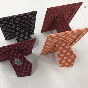 May include: Four different picture frames with a variety of college team logos. The frames are made of fabric and have a stand on the back. The logos are for the University of Alabama, Auburn University, the University of Georgia, and Clemson University.