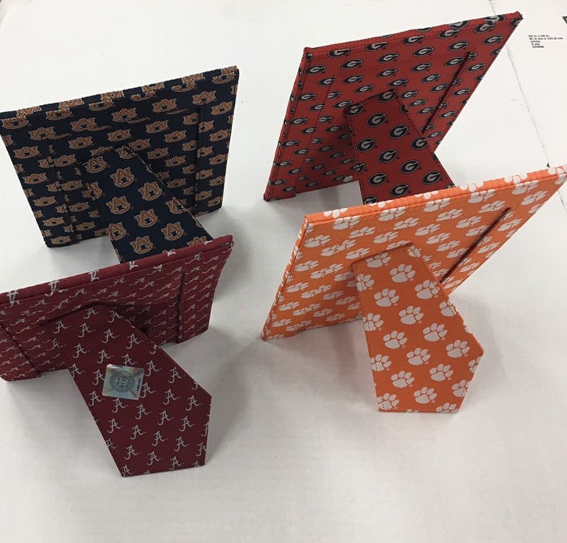 May include: Four different picture frames with a variety of college team logos. The frames are made of fabric and have a stand on the back. The logos are for the University of Alabama, Auburn University, the University of Georgia, and Clemson University.