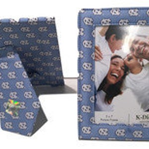 May include: A blue picture frame with a white and blue pattern. The frame is 4x6 inches and has a stand on the back. The frame is made by K. Carter.
