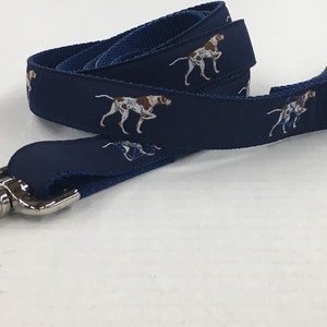 May include: A blue dog leash with a silver clip. The leash has a repeating pattern of brown and white dogs.
