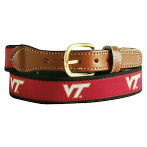 May include: A brown leather belt with a gold buckle and a red and black woven strap. The strap features the letters "VT" in white.