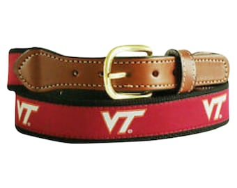 May include: A brown leather belt with a gold buckle and a red and black woven strap. The strap features the letters "VT" in white.