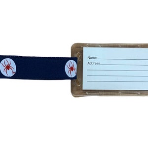 May include: A clear plastic luggage tag with a dark brown strap. The strap has two white circles with red spider silhouettes. The tag has the words "Name" and "Address" printed on it.