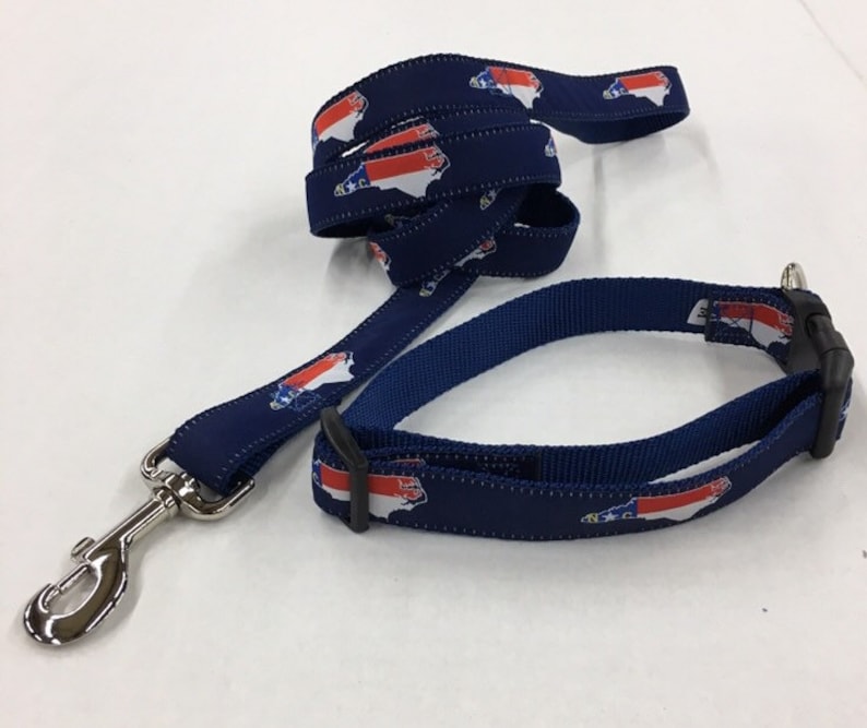 Op de afbeelding: Een blauwe hondenriem en halsbandset met een herhalend patroon van de omtrek van de staat North Carolina in rood, wit en blauw.