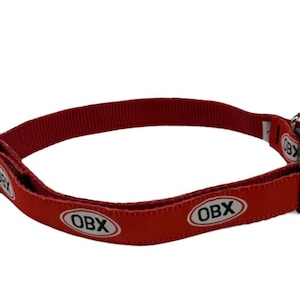 Op de afbeelding: Rode hondenriem met een zwarte gesp en de tekst "OBX" drie keer herhaald in witte ovale vormen.