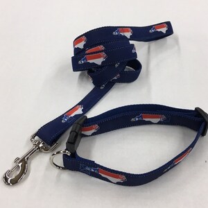 Op de afbeelding: Een blauwe hondenriem en halsband met een herhalend patroon van de staat North Carolina in rood, wit en blauw.