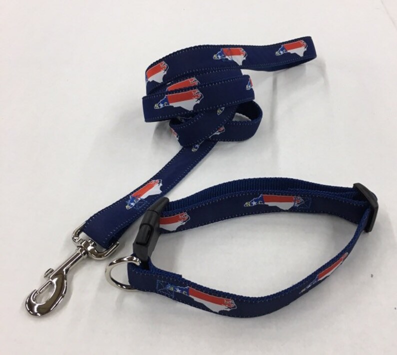 Op de afbeelding: Een blauwe hondenriem en halsband met een herhalend patroon van de staat North Carolina in rood, wit en blauw.