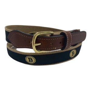 May include: A black and tan woven belt with a brown leather buckle and gold-colored Bitcoin symbols.