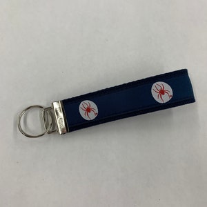 May include: A dark blue key chain with a silver key ring and two white circles with red spider designs.