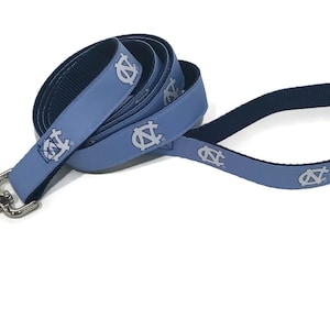 May include: A light blue dog leash with a silver metal clasp. The leash features a repeating pattern of a white logo. The leash is made of a durable material and is designed for pet owners.