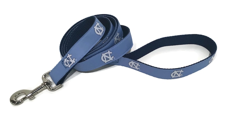May include: A light blue dog leash with a silver metal clasp. The leash features a repeating pattern of a white logo. The leash is made of a durable material and is designed for pet owners.