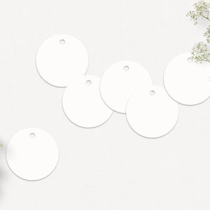 May include: Six blank white round gift tags with holes for string or ribbon. The tags are arranged in a semi-circle on a white background.