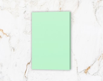 May include: A light green blank card on a white marble background.