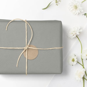 May include: A gray gift box wrapped in brown paper with a brown paper tag and tied with twine. The box is surrounded by white flowers with green stems.
