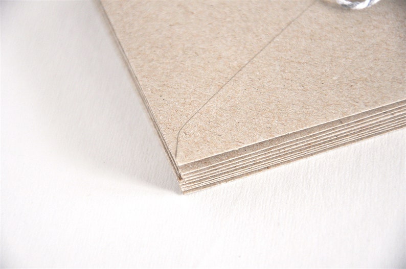 May include: A stack of brown kraft paper envelopes with a white string attached to the top.