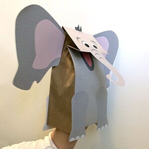 Puede incluir: Un t&iacute;tere de papel gris con forma de elefante con orejas de papel marr&oacute;n y una trompa de papel marr&oacute;n. El elefante tiene una cara gris con ojos negros y una boca roja.