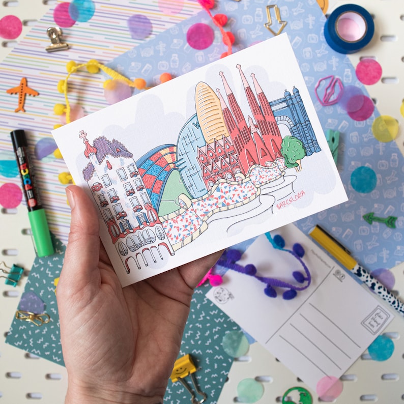 May include: A postcard with a colorful illustration of the Barcelona skyline, including the Sagrada Familia, Park G&uuml;ell, and other iconic landmarks. The postcard is white with a light blue border and the word "Barcelona" printed in black at the bottom.