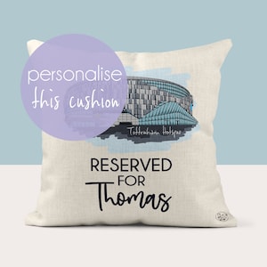May include: A white cushion with a watercolor illustration of Tottenham Hotspur Stadium. The text "RESERVED FOR Thomas" is printed on the cushion.