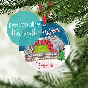 May include: A round Christmas ornament with a blue and white background featuring a cartoon illustration of a soccer stadium. The ornament has the text "Christmas Wishes" and "Joshua" on it.