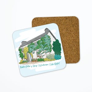 May include: A square coaster featuring an illustration of a white house with a gray roof, surrounded by green and yellow foliage. The text "Beatrix Potter's House | Windermere | Lake District" is at the bottom. A cork coaster is behind it.