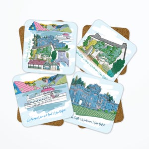 May include: Set of four square coasters with illustrations of the Lake District. Each coaster features a different scene, including a boat, castle, and buildings, with the text "Windermere | Lake District". The coasters are on a cork base.