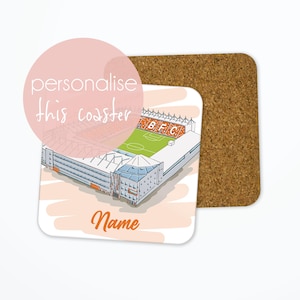 May include: A white coaster with a drawing of a football stadium in orange and white. The text "personalise this coaster" and "Name" are on the coaster. The coaster is on top of a cork coaster.