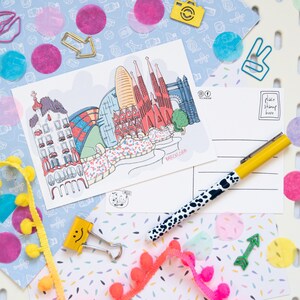 May include: A colorful postcard with a hand-drawn illustration of the Sagrada Familia basilica in Barcelona, Spain. The postcard has a place to put a stamp and an address. The text on the postcard says "Barcelona".