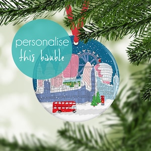 May include: A round ceramic Christmas ornament featuring a detailed illustration of the London skyline in winter, including the London Eye, Big Ben, and a red double-decker bus. The scene is set against a dark blue snowy background with a red ribbon.