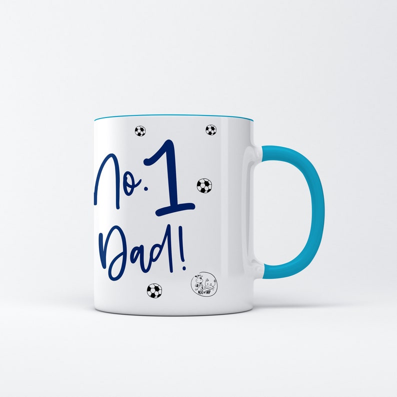 May include: White ceramic mug with a blue rim and handle. The mug has a blue inscription that reads "No. 1 Dad!" with soccer ball graphics.