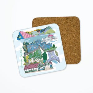 May include: A square coaster featuring a colorful illustration of Windermere in the Lake District. The design includes a blue castle, a lake, mountains, and a boat. The coaster is paired with a cork base.