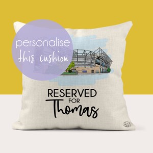 May include: A white cushion with a drawing of a stadium and the text "RESERVED FOR Thomas".