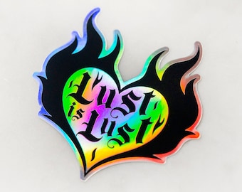 May include: A black and white heart-shaped sticker with flames on the sides. The heart has the words "Lust is Lust" written inside in a gothic font. The sticker is iridescent and has a rainbow sheen.