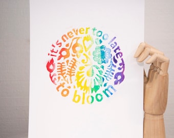 Puede incluir: Una tarjeta blanca con un diseño circular de arcoíris que presenta el texto "it's never too late to bloom".