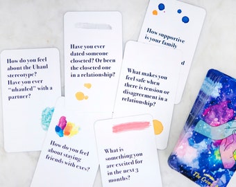 Puede incluir: Una baraja de cartas con un diseño de acuarela en la parte delantera. Las cartas tienen preguntas sobre las relaciones. El texto de las cartas está en azul. La baraja se llama "The Crown Art".