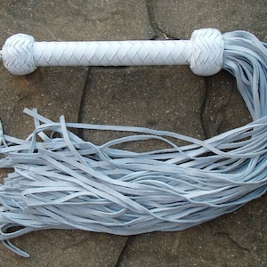 May include: A white leather bullwhip with a braided handle and a long, fringed tail.