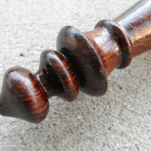 May include: A dark brown wooden finial with a rounded tip and a series of concentric rings. The finial has a smooth, polished finish.