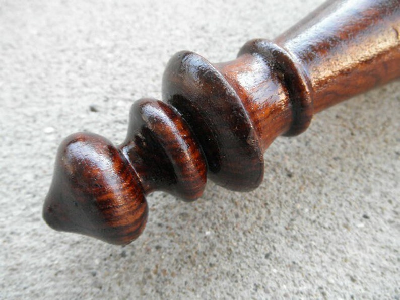 May include: A dark brown wooden finial with a rounded tip and a series of concentric rings. The finial has a smooth, polished finish.