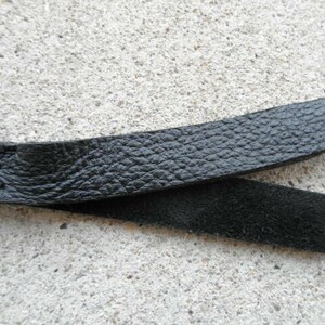 May include: A black leather whip with a braided handle and a smooth, textured surface.