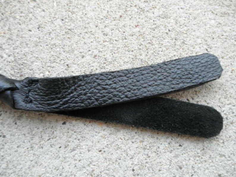 May include: A black leather whip with a braided handle and a smooth, textured surface.