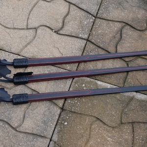 May include: Three black leather whips with red stitching. The whips are laid out on a gray concrete surface.