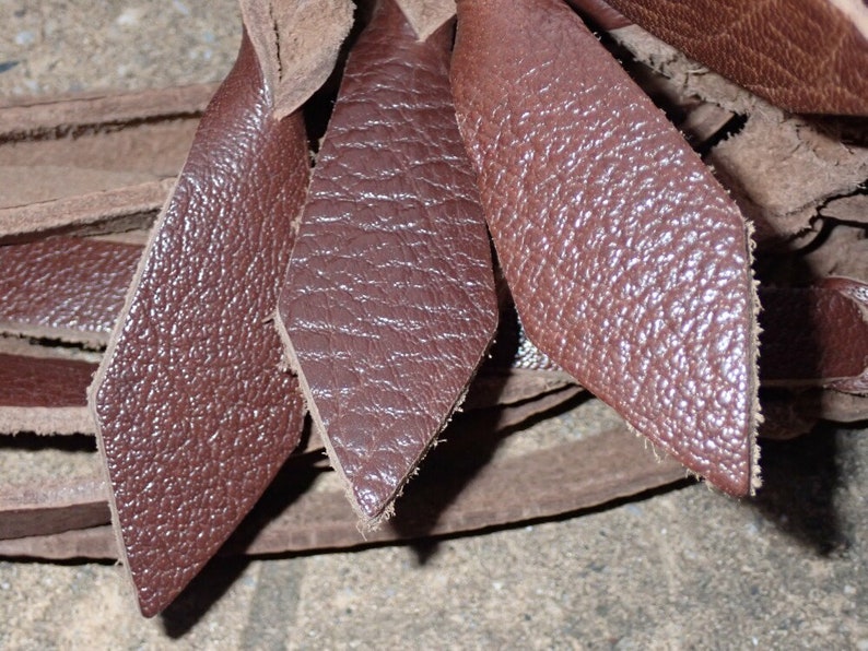 May include: Close-up of several diamond-shaped pieces of brown leather. The leather has a textured surface and appears to be cut from a larger piece. The edges of the leather are rough, and the pieces are overlapping.