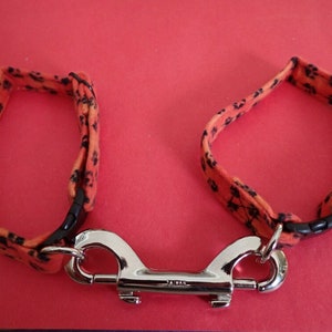 May include: Orange and black dog collar with paw print design and a silver metal clip.