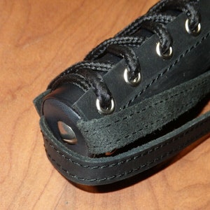 May include: Close-up of a black leather object with a lace-up design and silver eyelets. The object has a strap and is stitched with black thread. The leather appears to be textured.